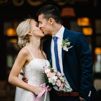 Portrait of an attractive bride who embraces the groom and holding bouquet of pink and purple flowers and greens with ribbon at the wedding ceremony.